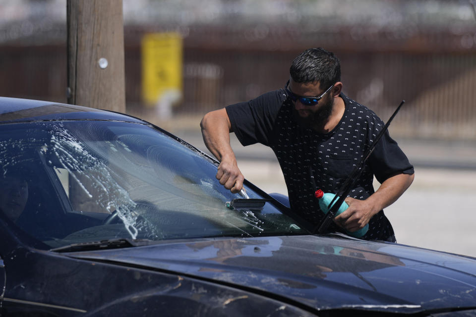 Irwing Lopez, a 35-year-old migrant construction worker from Venezuela, washes windshields for tips at a stoplight near the U.S. border wall, behind, in Ciudad Juarez, Mexico, Thursday, March 30, 2023. Lopez's friend and fellow Venezuelan Samuel Marchena was detained by immigration agents and hours later became one of the 39 migrants who died earlier this week in a fire at an immigration detention center. (AP Photo/Fernando Llano)