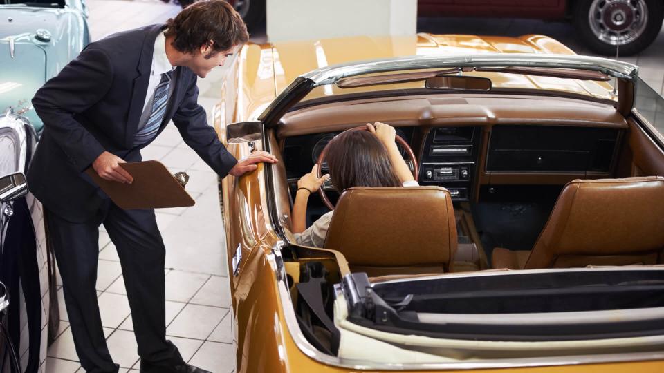 Handsome young classic car salesman standing in the dealership and helping a client make a decision.