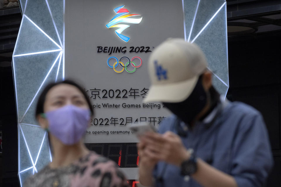 People wearing face masks to protect against COVID-19 walk past a display showing a countdown clock to the Beijing 2022 Winter Olympics in Beijing, Wednesday, Aug. 18, 2021. China's "zero tolerance" strategy of trying to isolate every case and stop transmission of the coronavirus has kept kept the country where the virus first was detected in late 2019 largely free of the disease. (AP Photo/Mark Schiefelbein)