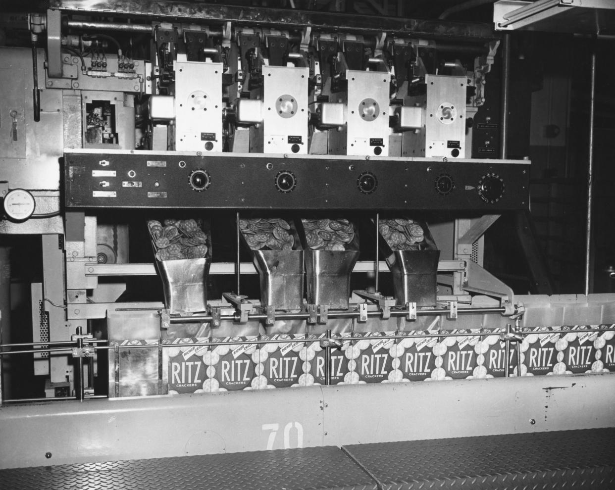 Machinery at a Ritz Cracker packing facility, with crackers pouring into a hopper which is then dispensed into each carton, U.S., vintage black and white image, circa 1950
