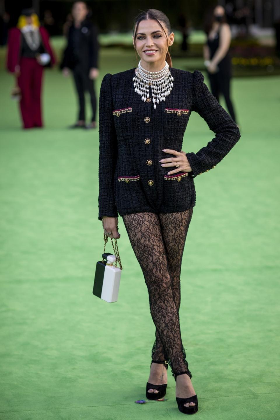 A woman in a black, button-down jacket and lace pants posing on a green carpet