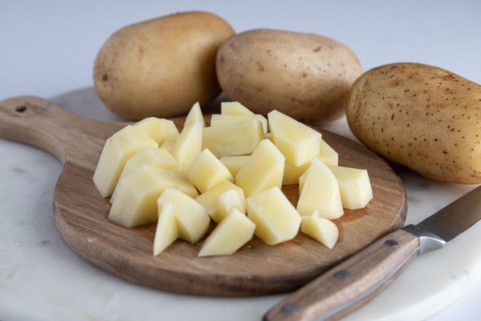 a wooden cutting board with several peeled and sliced potatoes placed atop it