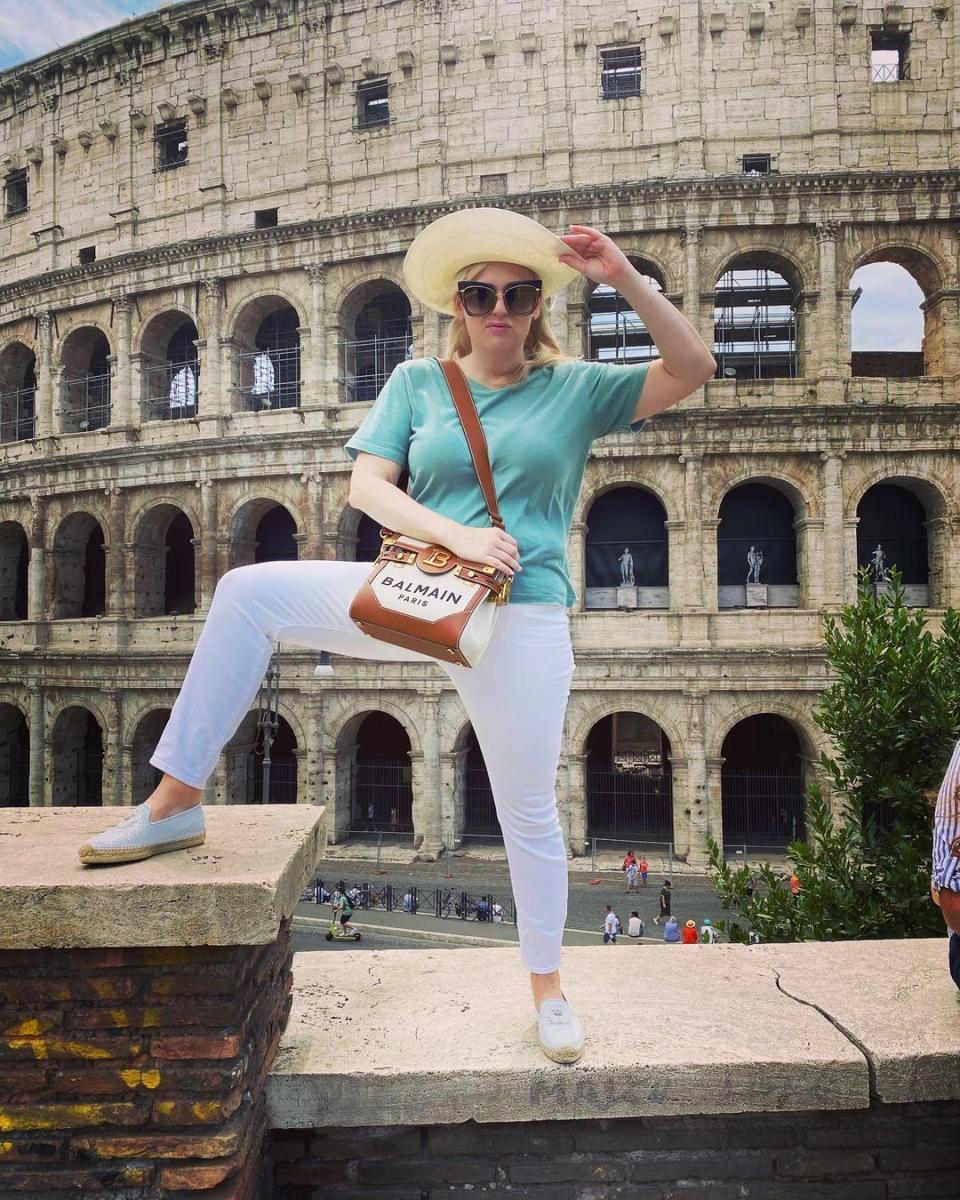 Rebel Wilson wearing a blue t-shirt and white jeans while standing in front of the Colosseum in Rome. Photo: Instagram/rebelwilson.