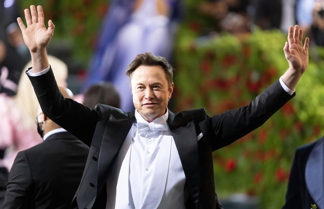 Elon Musk greets onlookers with both hands waving, at the 2022 Met Gala