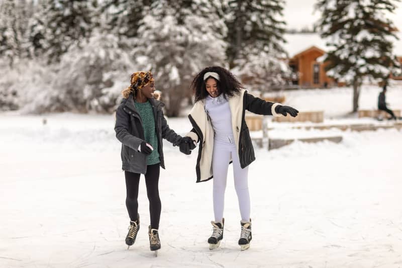 Women hold hands for balance as they learn to ice-skate on frozen lake