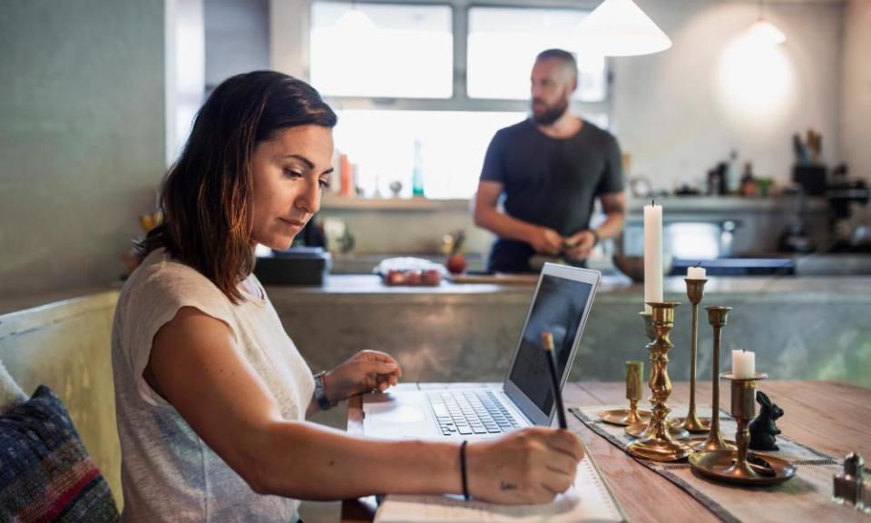 woman uses laptop at home with man in background