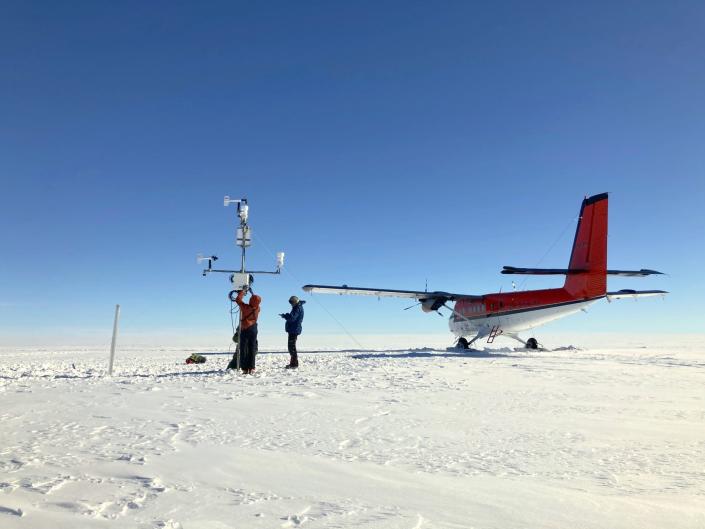 A glaciologist team for the Geological Survey of Denmark and Greenland sets up an automatic weather station on the snowy surface above the snow line during the melt season.
