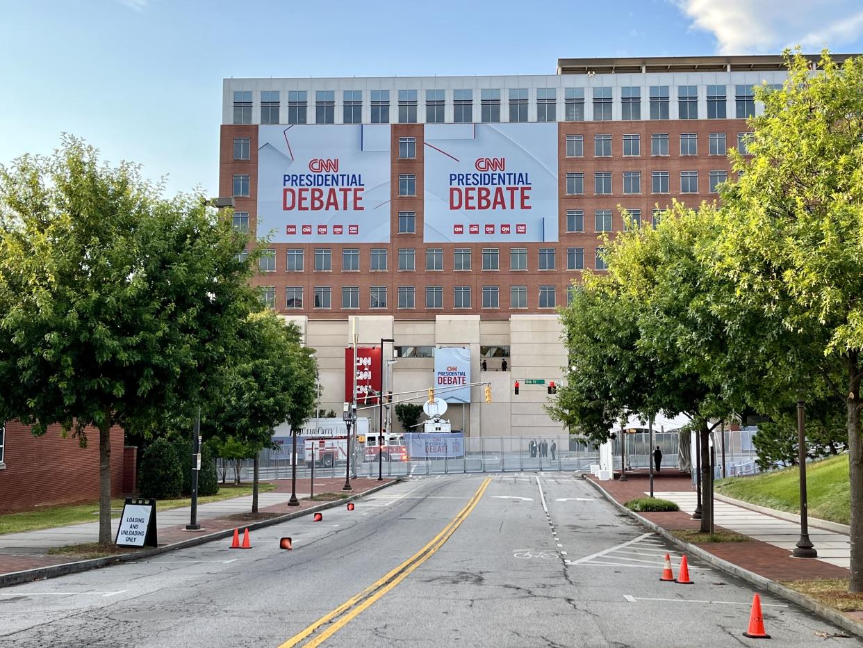 Large building at the end of an orange-cone-lined road ending with chain link fence. The building has large signs reading: CNN presidential debate