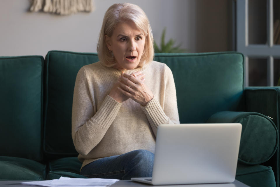 Shocked grey haired mature woman with wide opened eyes reading unexpected online news on laptop, sitting on couch, looking at screen, stressed middle aged female receiving bad email, computer problem