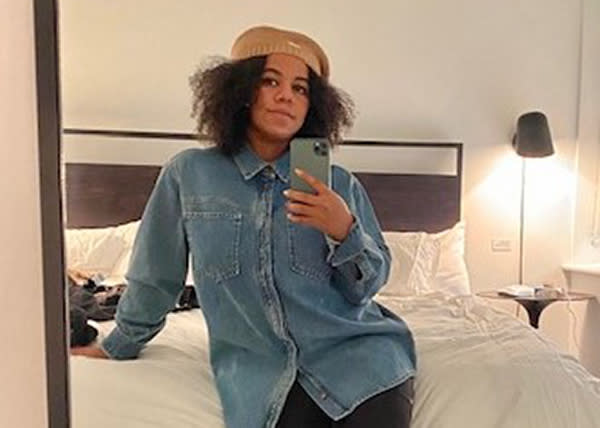 Home photo of ShaLisa Pratt shows her taking a selfie in a mirror as she sits on a double bed.