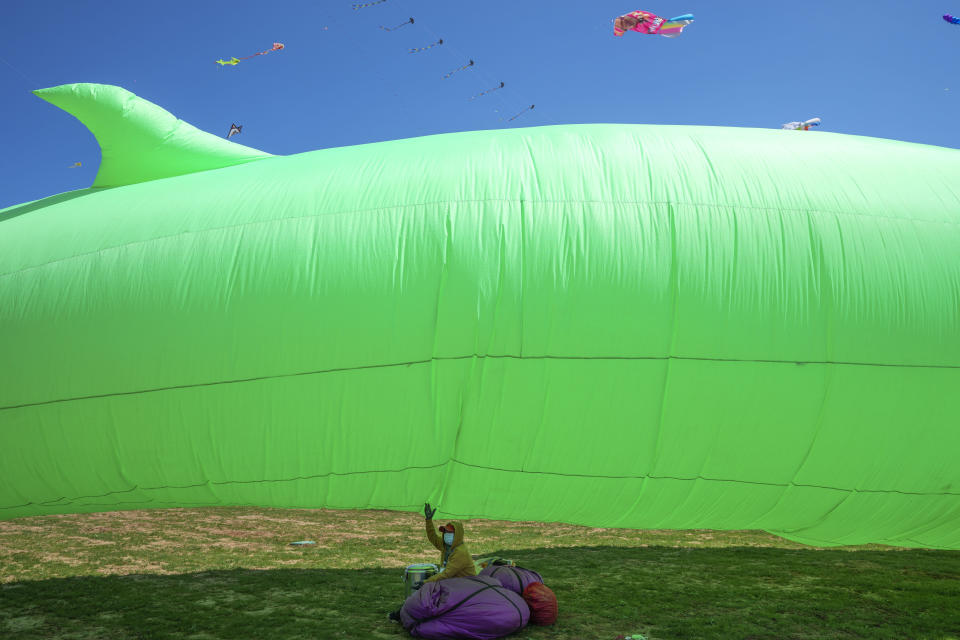 A participant sits under a kite during the 41st International Kite Festival in Weifang, Shandong Province of China, Saturday, April 20, 2024. (AP Photo/Tatan Syuflana)