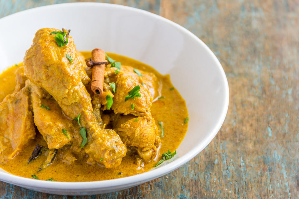 A bowl of chicken curry garnished with coriander and a stick of cinnamon