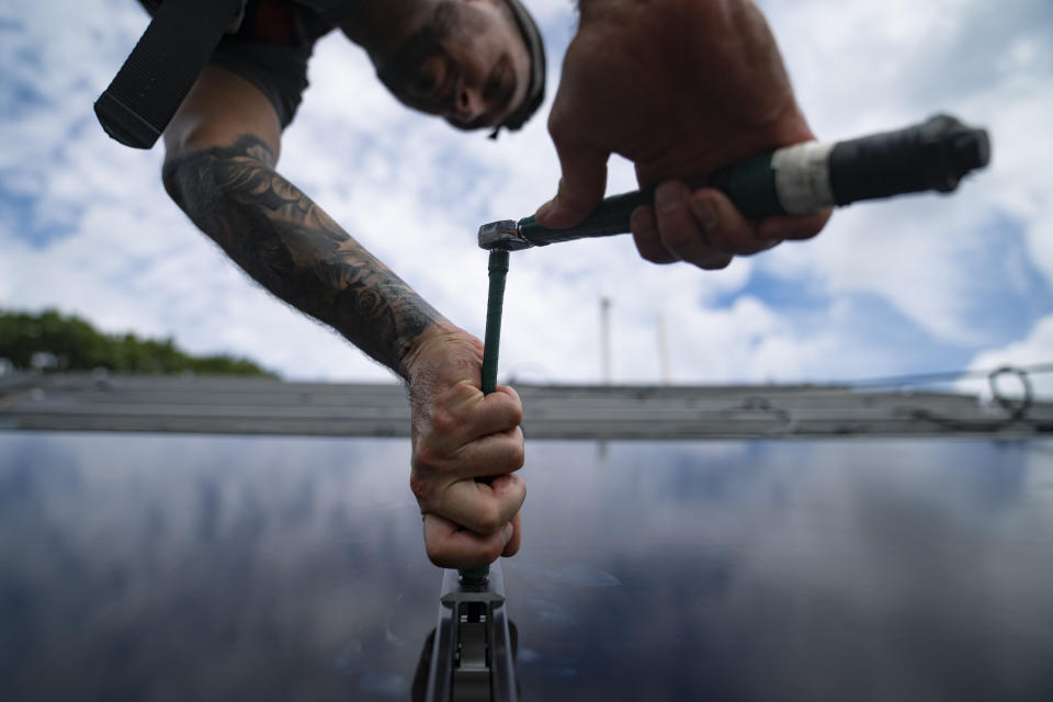 FILE - An employee of NY State Solar, a residential and commercial photovoltaic systems company, installs an array of solar panels on a roof, Aug. 11, 2022, in Massapequa, N.Y. Across Europe companies are weighing up the U.S. Inflation Reduction Act's $375 billion in benefits for renewable industries against the European Union's fragmented response. (AP Photo/John Minchillo, File)