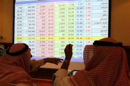 Saudi men look to a screen showing stock prices at ANB Bank, in Riyadh