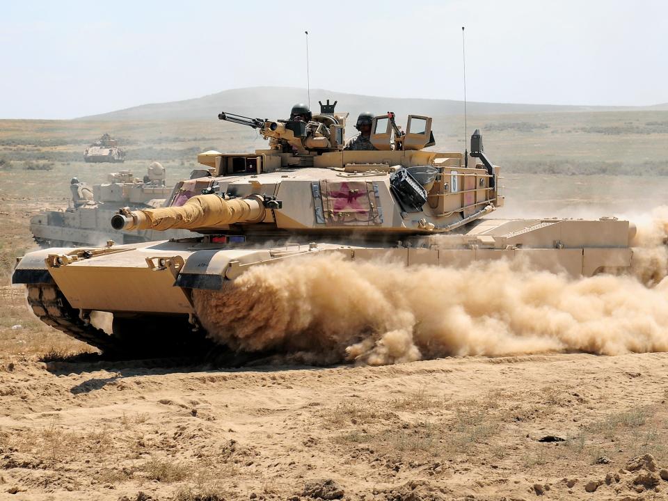 An M1A2 Abrams main battle tank from the Minnesota National Guard races through a breach in a barbed wire obstacle during the 116th eXportable Combat Training Exercise at the Orchard Combat Training Center, Idaho