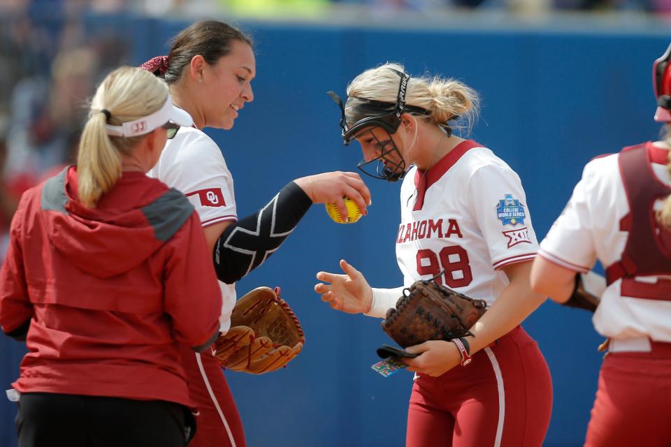 OU's Hope Trautwein (7) hands the ball to Jordyn Bahl (98) as she enters the game to pitch in the fifth inning of a 13-2 win against Northwestern in the WCWS.