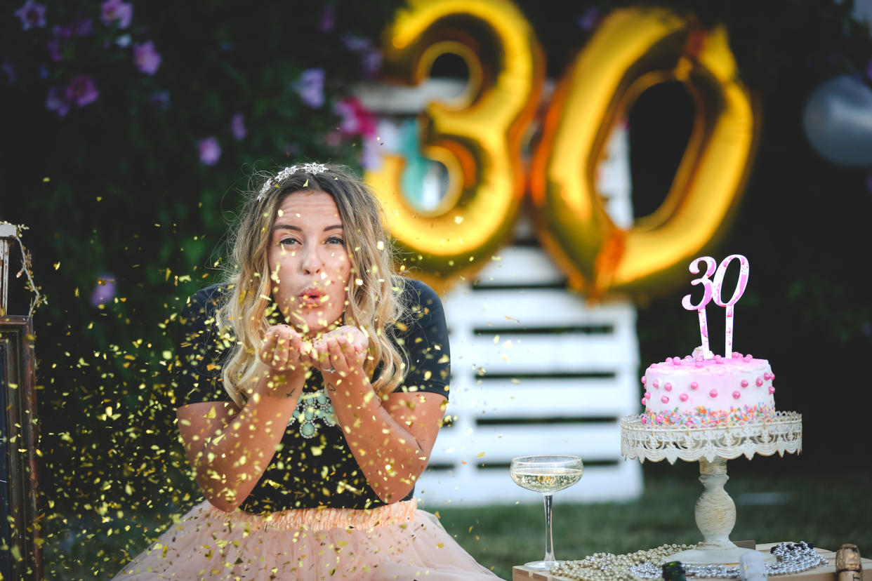 A woman blowing confetti at the camera while celebrating her 30th birthday.