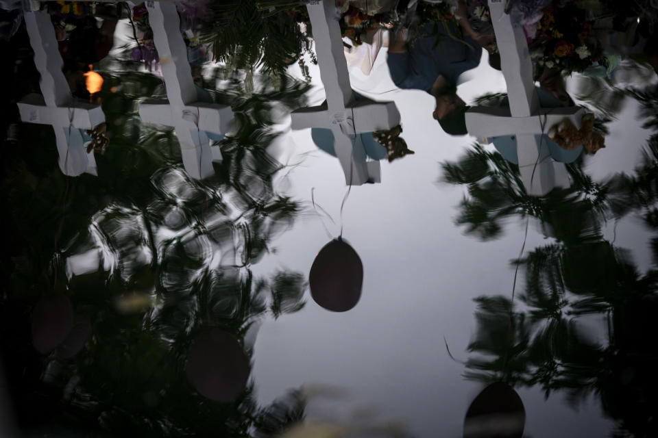 Crosses and balloons are seen reflected in a water fountain at the town square on Thursday, May 26, 2022, in Uvalde, Texas. In a town as small as Uvalde, even those who didn't lose their own child lost someone. Some say now that closeness is both their blessing and their curse: they can lean on each other to grieve. But every single one of them is grieving. (AP Photo/Wong Maye-E)