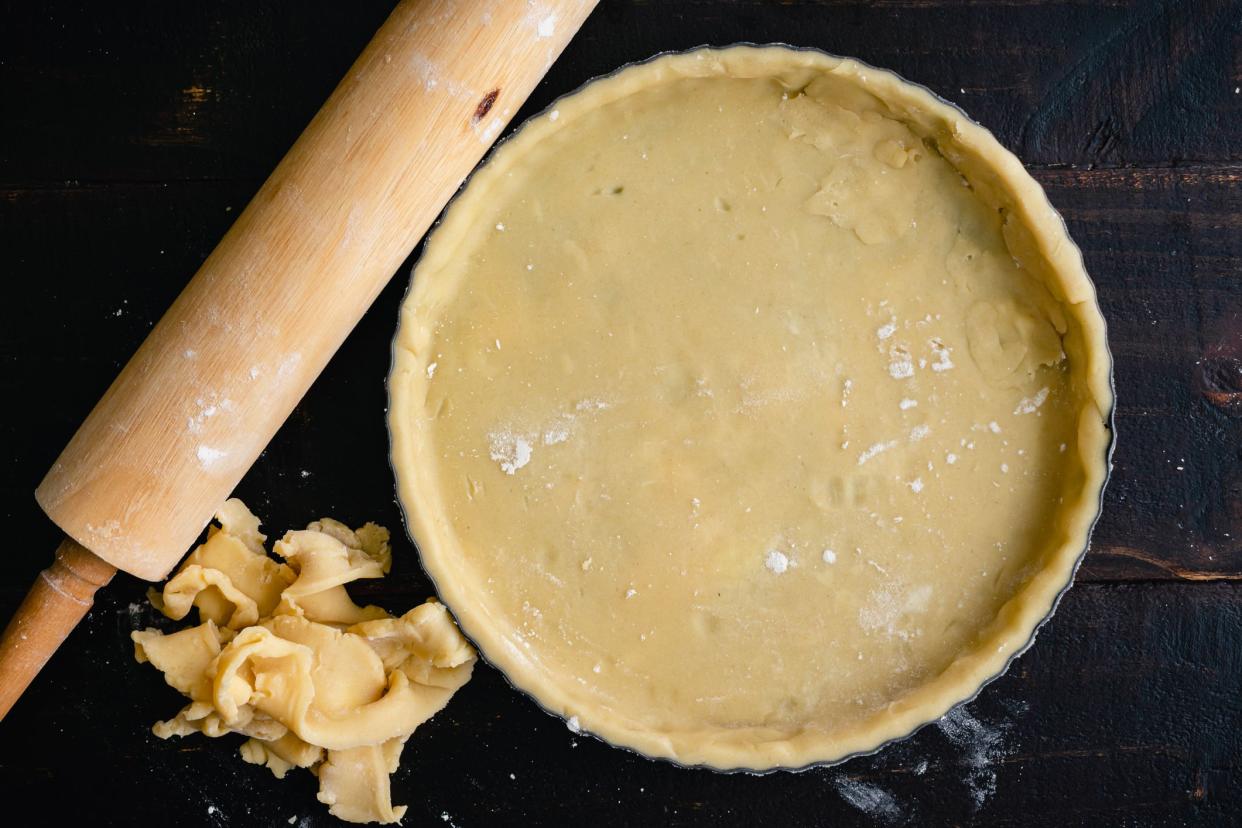 Dough-filled tart pan with pastry crust scraps and a rolling pin