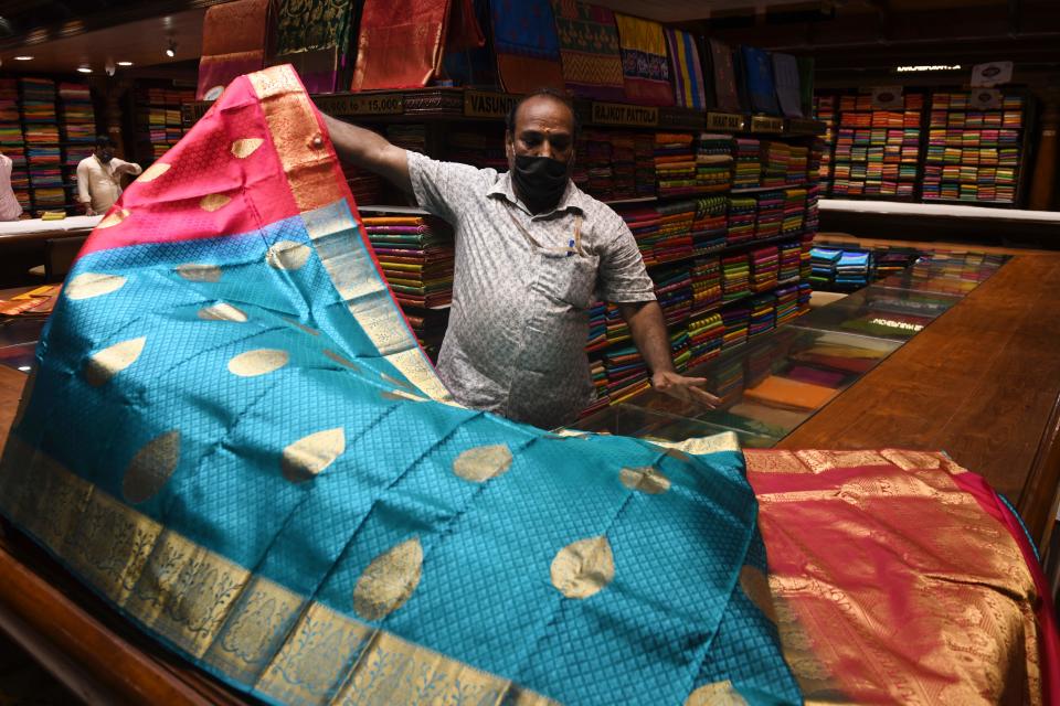 A salesman wearing a facemask shows sarees to customers at a textile garments shop in Chennai on June 1, 2020. (Photo by ARUN SANKAR/AFP via Getty Images)