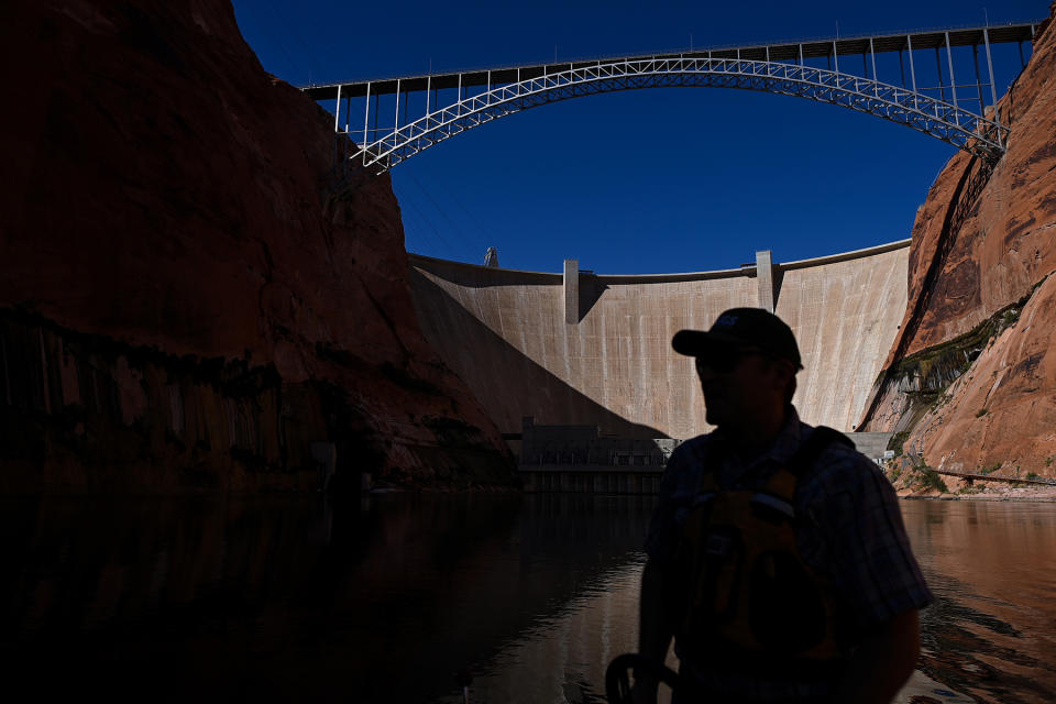 PAGE, AZ - OCTOBER 14: United States Geological Survey Research Ecologist Ted Kennedy drives his boat along the Colorado River as the The Glen Canyon Dam is seen in the background on October 14, 2022 in Page, Arizona. The water in Lake Powell and the Colorado River has been receding due to recent droughts leaving parts of the lake and river parched. The federal government are moving forward with plans to reduce water allocations from the Colorado River Basin to Arizona and is asking millions of residents to reduce their water consumption as the drought get worse. (Photo by Joshua Lott/The Washington Post via Getty Images)