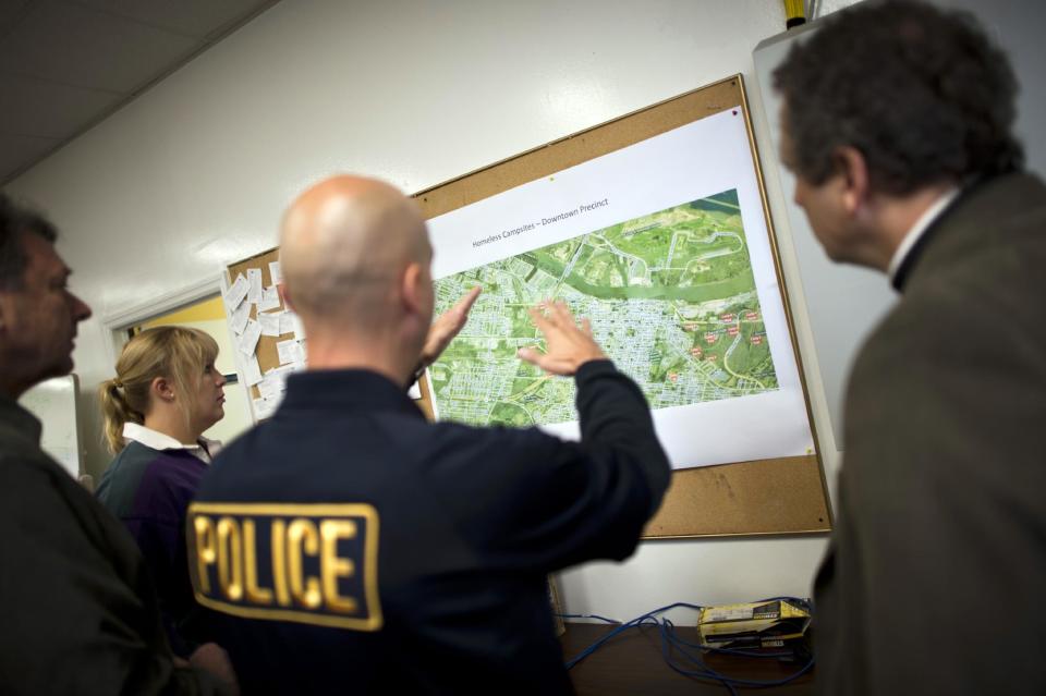 In this Monday, Dec. 9, 2013 photo, Homeless Liaison Officer Tom Gentner, center, uses a map to show a group from the Episcopal Diocese of Georgia where they plan to hold a Christmas service in Camp 8 South under the Truman Parkway, in Savannah, Ga. Since being named homeless liaison in 2013, Gentner designated camp boundaries by using features in the terrain, numbering each one to help emergency services with locations. (AP Photo/Stephen Morton)