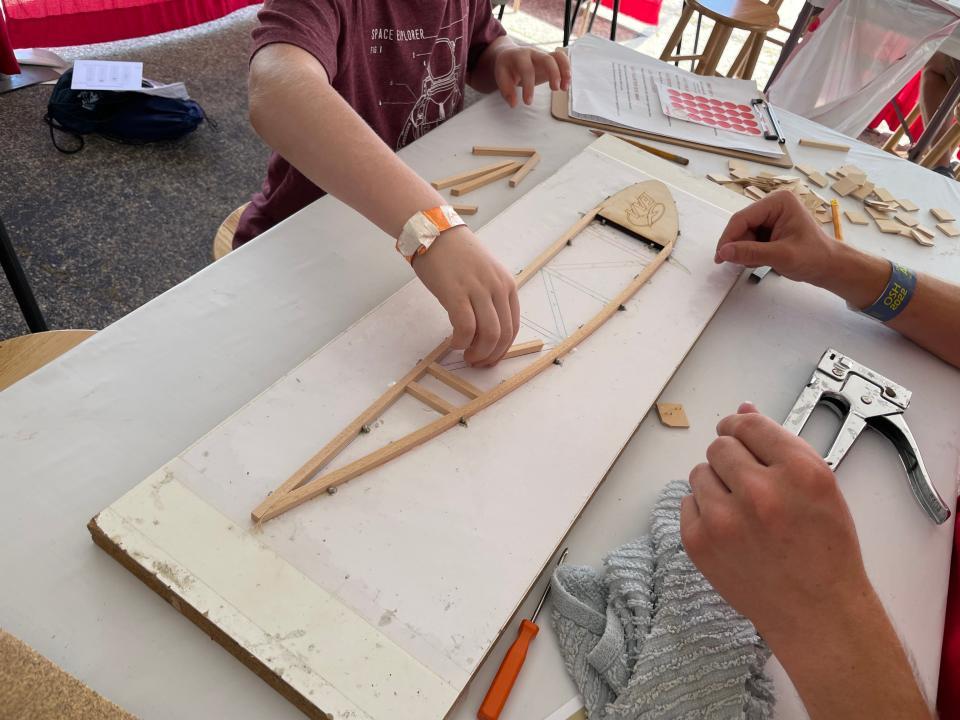 A volunteer helps a child build a wing rig using wood pieces, glue and staples at KidVenture at EAA AirVenture on July 25, 2022.