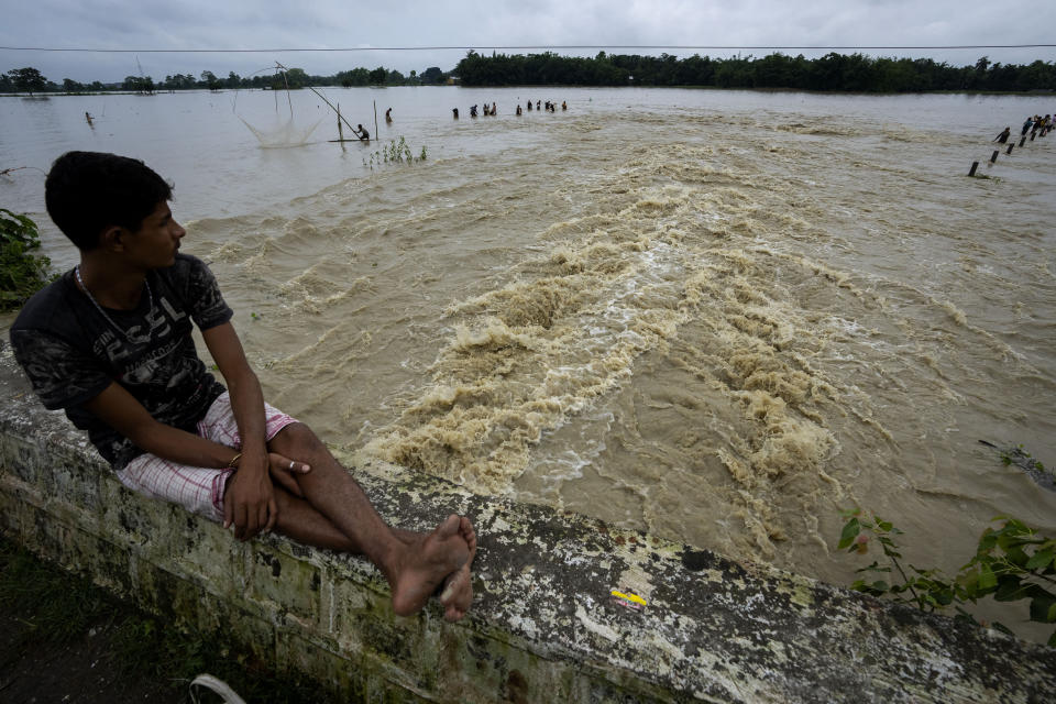 A boy watches people fishing in floodwaters in Korora village, west of Gauhati, India, Friday, June 17, 2022. (AP Photo/Anupam Nath)