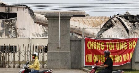 Residents ride past the damaged Taiwanese-owned Alhonga factory in Vietnam's southern Binh Duong province May 16, 2014. REUTERS/Stringer