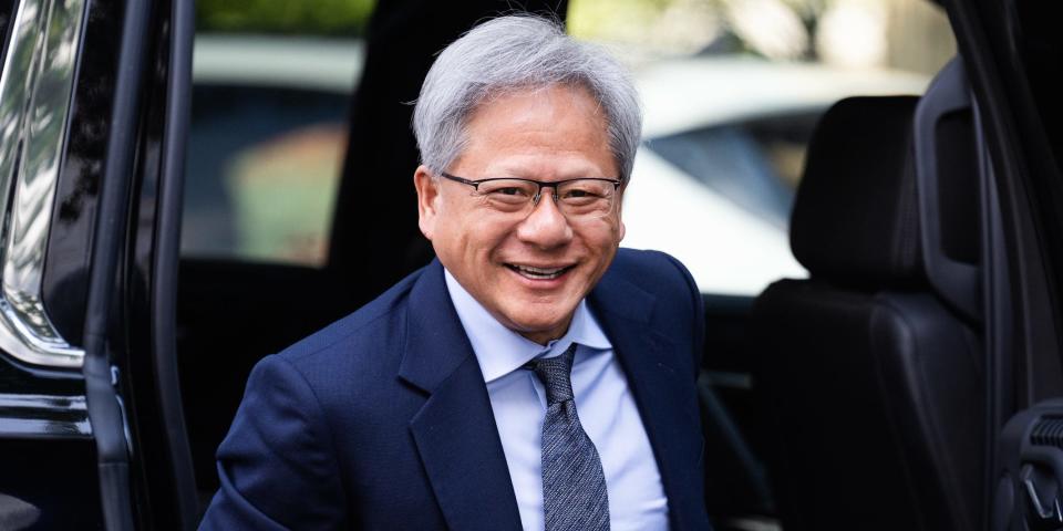 Jensen Huang smiling whilst wearing a navy blue suit, light blue shirt and dark blue tie