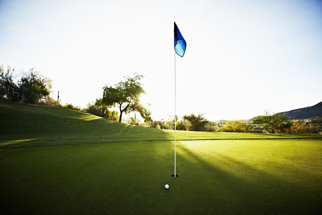 Golf ball next to flag on putting green on golf course at sunrise