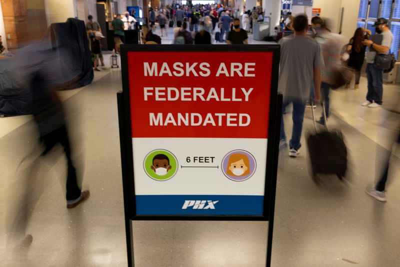 FILE PHOTO: Air travelers make their way past a sign mandating face masks for all during the outbreak of the coronavirus disease (COVID-19) in Phoenix