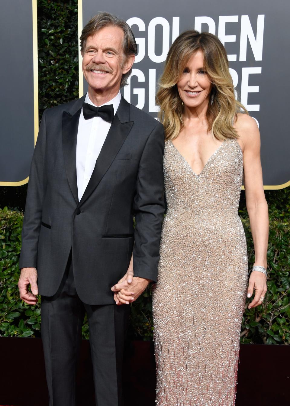 Two people posing. One is wearing a black tuxedo and the other is wearing a sequined V-neck dress