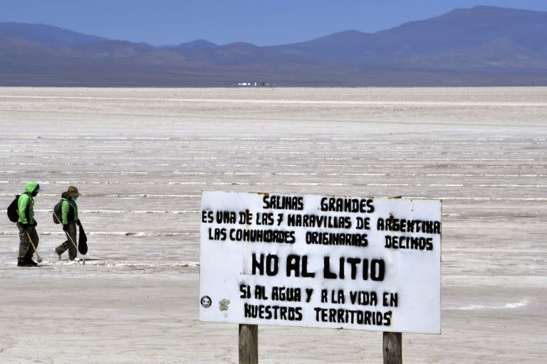 A sign against the exploitation of lithium is seen as employees work at the Salinas Grandes salt flat, shared by the Argentine northern provinces of Salta and Jujuy, near the Kolla indigenous community of Santuario de Tres Pozos, which in 2019 expelled two mining companies from the salt flat, in Jujuy, on October 18, 2022. - The turquoise glimmer of open-air pools meets the dazzling white of a seemingly endless salt desert where hope and disillusionment collide in Latin America's "lithium triangle." A key component of batteries used in electric cars, demand has exploded for the "white gold" found in Argentina, Bolivia and Chile in quantities larger than anywhere else in the world. (Photo by Aizar RALDES / AFP)