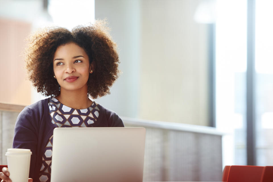 Career woman sitting at a laptop with a coffee looking into the distance