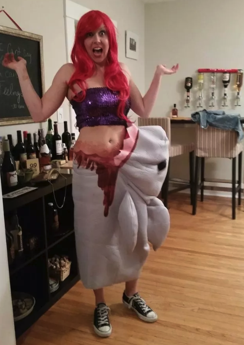 A woman dressed as Ariel but with the bottom half of her body covered in blood and a cloth-made shark