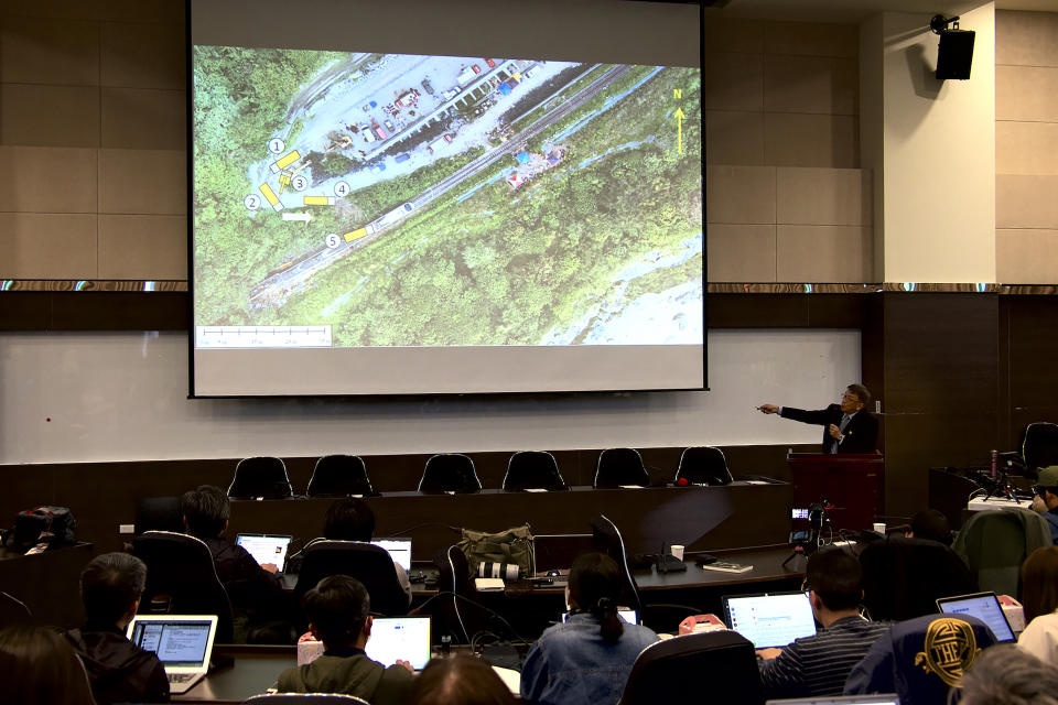 Yang Hong-chih, director of Taiwan Transportation Safety Board, at right, points to an aerial view of the site of the train derailment during a press conference held in Taipei, Taiwan on Tuesday, April 6, 2021. Investigators looking into Taiwan's deadliest railway disaster in decades combed through the crushed wreckage and debris for three days before they found the microSD chip from the dashboard camera of a construction truck that collided with a train coming out of a tunnel, officials said Tuesday. (AP Photo/Johnson Lai)