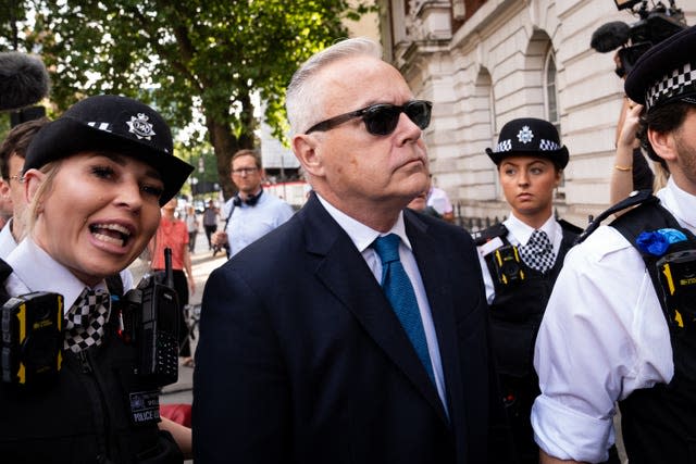 A man in a dark suit and sunglasses if flanked by female police officers