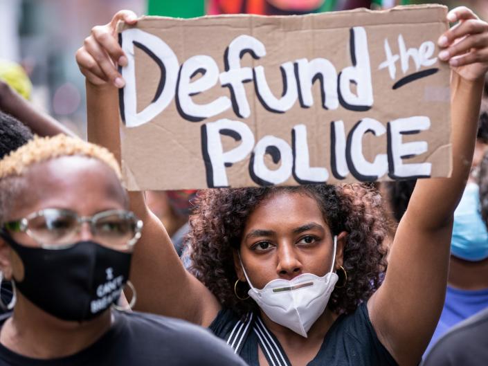 A protester wears a mask and holds a homemade sign that says &#34;Defund the Police&#34; at a demonstration on June 19, 2020, in New York City.