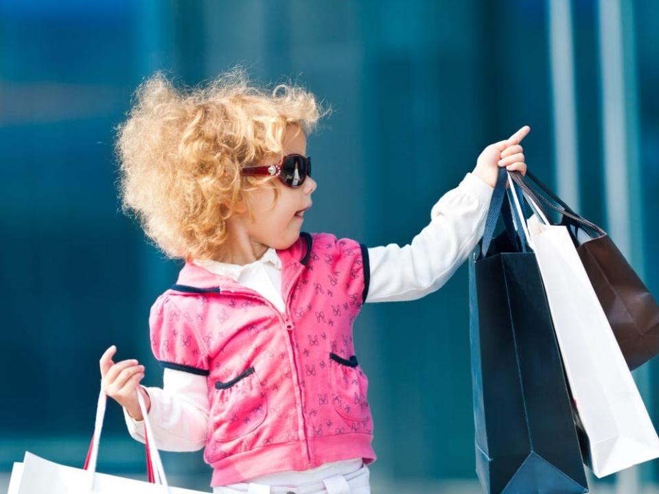 A little girl wearing sunglasses and holding shopping bags