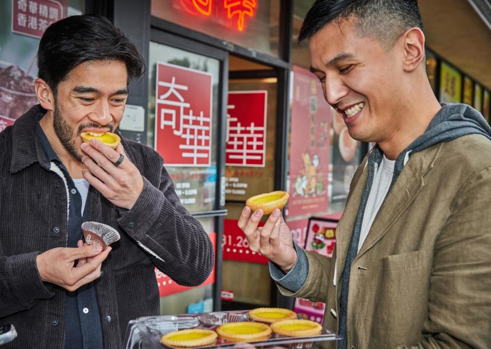 Justin Chien and Byron Wu eating egg tarts from Kee Wah Bakery.