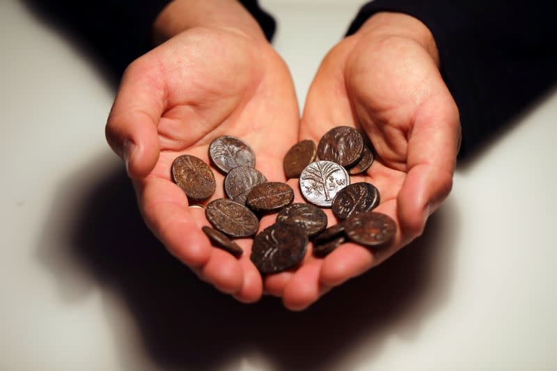 An employee holds ancient coins, part of various artefacts recently discovered in the Judean Desert caves along with scroll fragments of an ancient biblical texts, during an event for media at Israel Antiquities Authority laboratories in Jerusalem