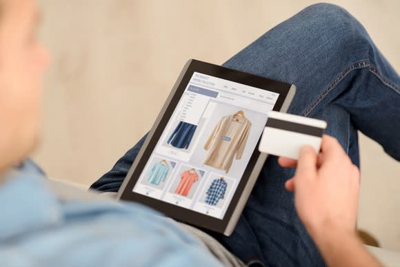 A man shops online using a tablet while holding a credit card.