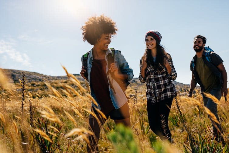 Three young friends walking through a field of wheat and smiling