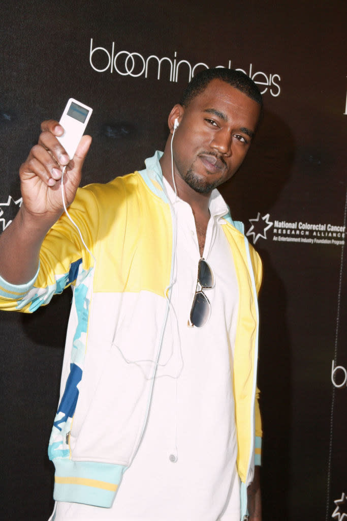 Kanye West holding up an iPod he's listening to with earbuds