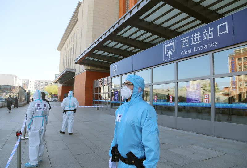 Police officers in protective suits are seen in front a closed entrance to a train station in Jilin