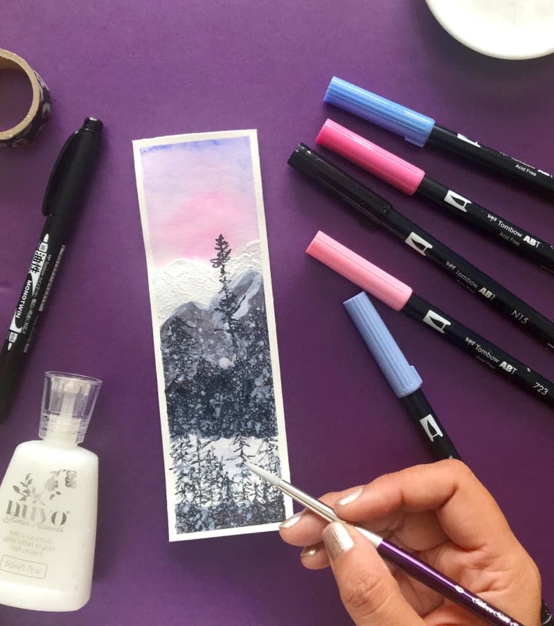 Hand decorating a bookmark next to different markers