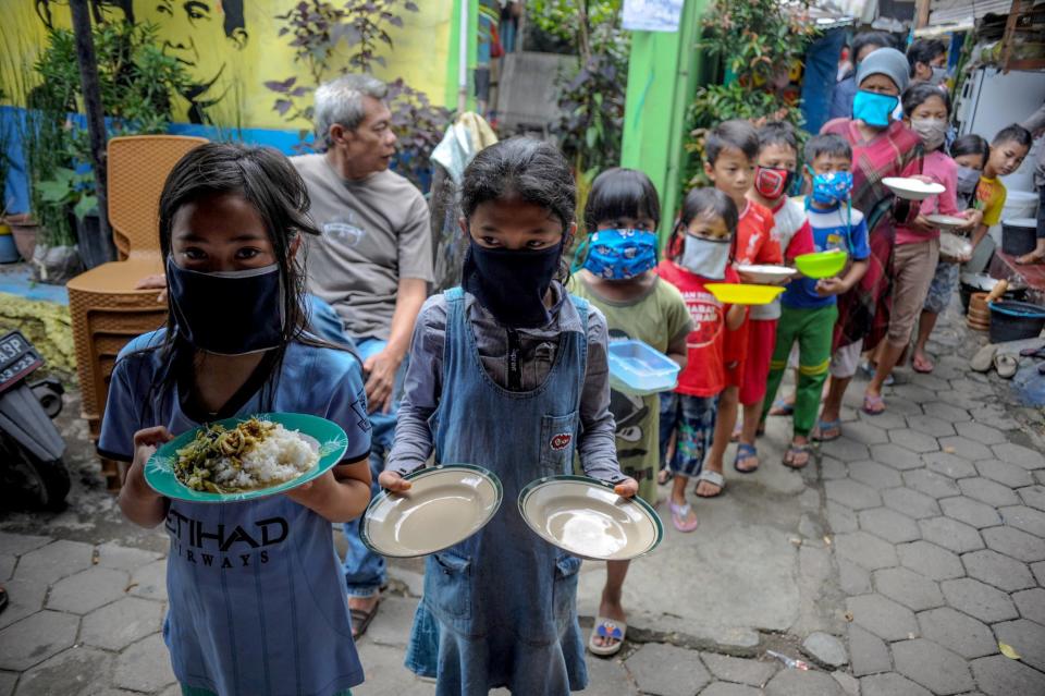 Locals wearing protective masks carry plates while queueing for food distributed for free amid the spread of coronavirus in Bandung, West Java province, on April 10.