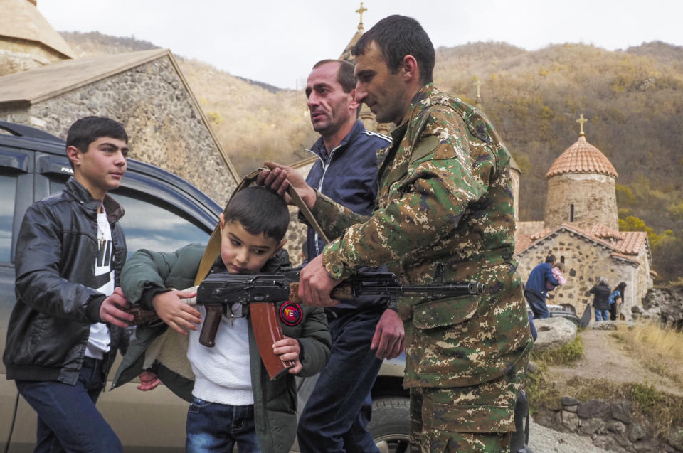 People shows a Kalashnikov gun to a boy at the Dadivank, an Armenian Apostolic Church monastery dating to the 9th century, as ethnic Armenians leave the separatist region of Nagorno-Karabakh to Armenia, Saturday, Nov. 14, 2020. The territory is to be turned over to Azerbaijan on Sunday as part of territorial concessions in an agreement to end six weeks of intense fighting with Armenian forces. Hundreds of thousands of Azeris were displaced by the war that ended in 1994. It is unclear when any civilians might try to settle in Karvachar — which will now be known by its Azeri name Kalbajar — or elsewhere. (AP Photo/Dmitry Lovetsky)