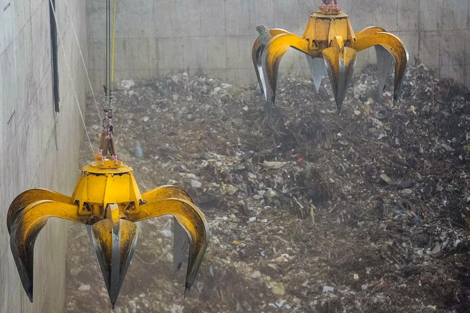 Crane-mounted claws grab piles of rubbish and plant debris from the pit floor of the new incinerator power generation facility at the Solid Waste Authority campus in West Palm Beach, Fla